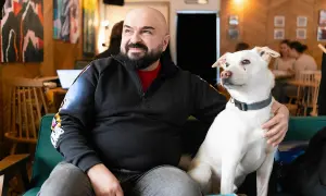 Łysy mężczyzna z brodą siedzi na kanapie z białym, dzikim psem.